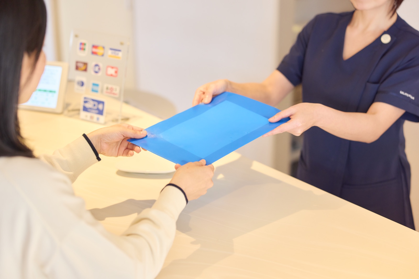 受付でスタッフから案内用トレーを受け取る患者さま