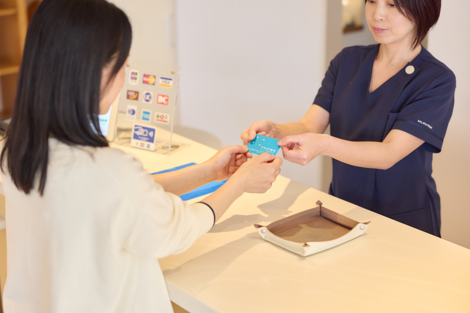 受付でスタッフから診察券を受け取る患者さま